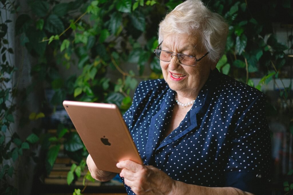 pexels-photo-5231330-5231330 Aged cheerful female smiling and using contemporary tablet while talking on tablet in living room with green plant